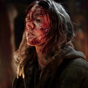 A bloodied woman stands in front of candles