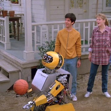 3 young people stand near a short, bulky robot that is holding a basketball