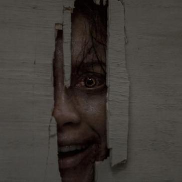 closeup of a possessed woman's face peering through a jagged hole in a door